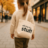 Child holding a tote bag with 'all my mini stuff' text on a city street.