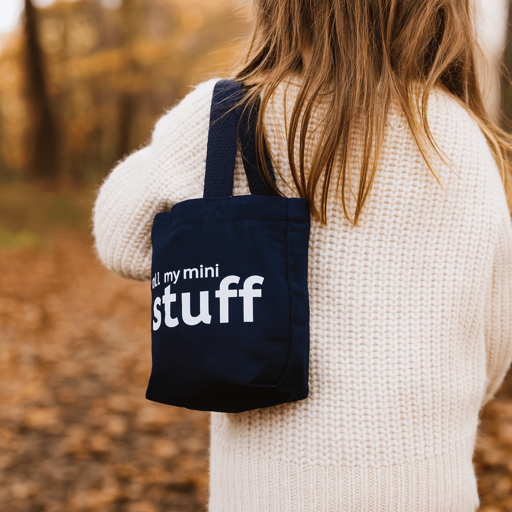 Person wearing a navy bag with 'all my mini stuff' text, standing outdoors.