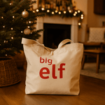 Natural tote bag with 'big elf' text in a festive room with a Christmas tree and fireplace.