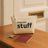 Natural pouch labeled 'important stuff' on a wooden surface with keys and a passport.