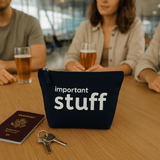 Navy pouch labeled 'important stuff' with passport and keys on a table, people in the background.