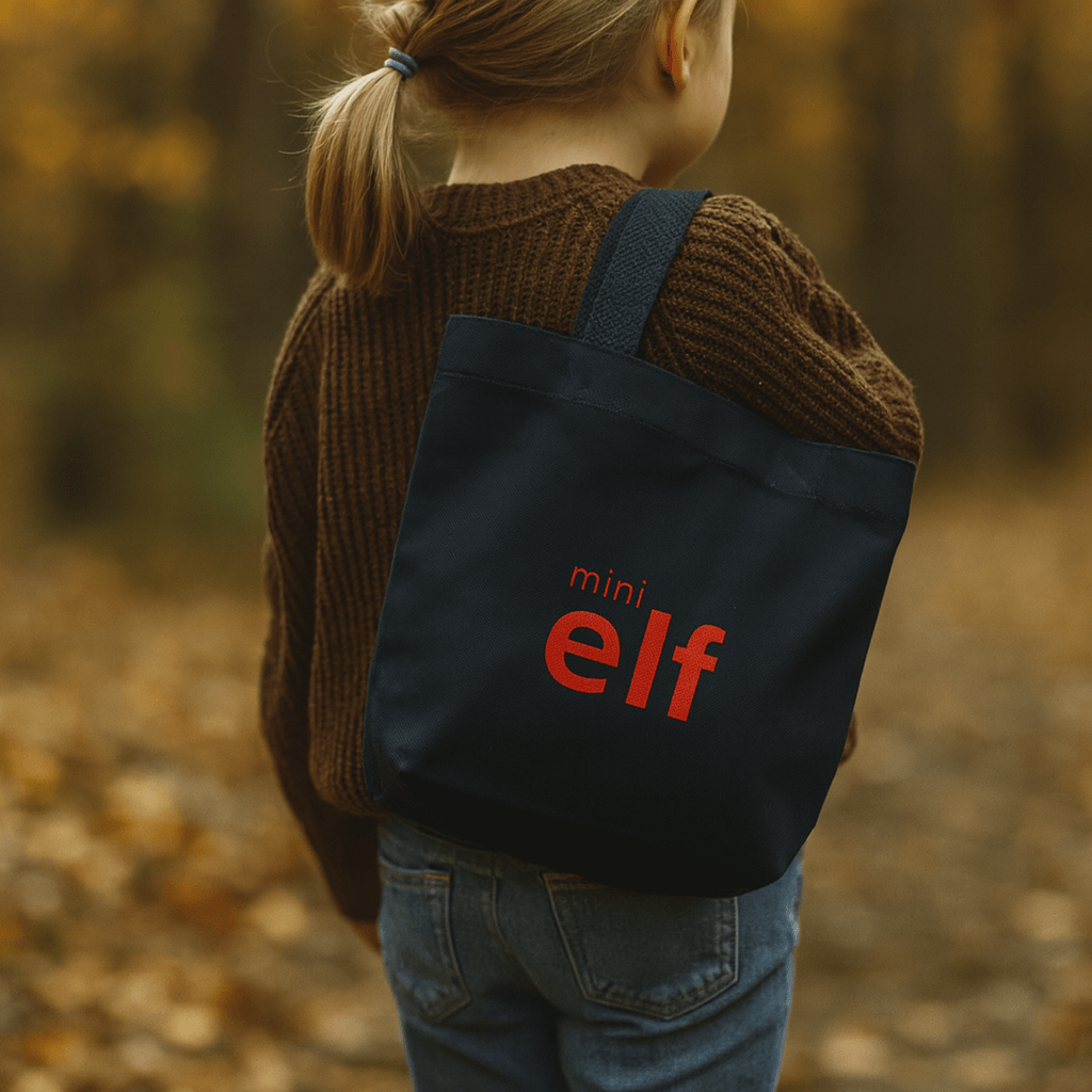 Girl wearing a navy tote with 'mini elf' text in an autumn setting