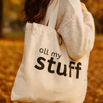Person holding a natural canvas tote bag with 'all my stuff' text in an outdoor autumn setting