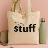 natural canvas tote bag with 'all my stuff' text, beige scarf, and green water bottle on a pink background