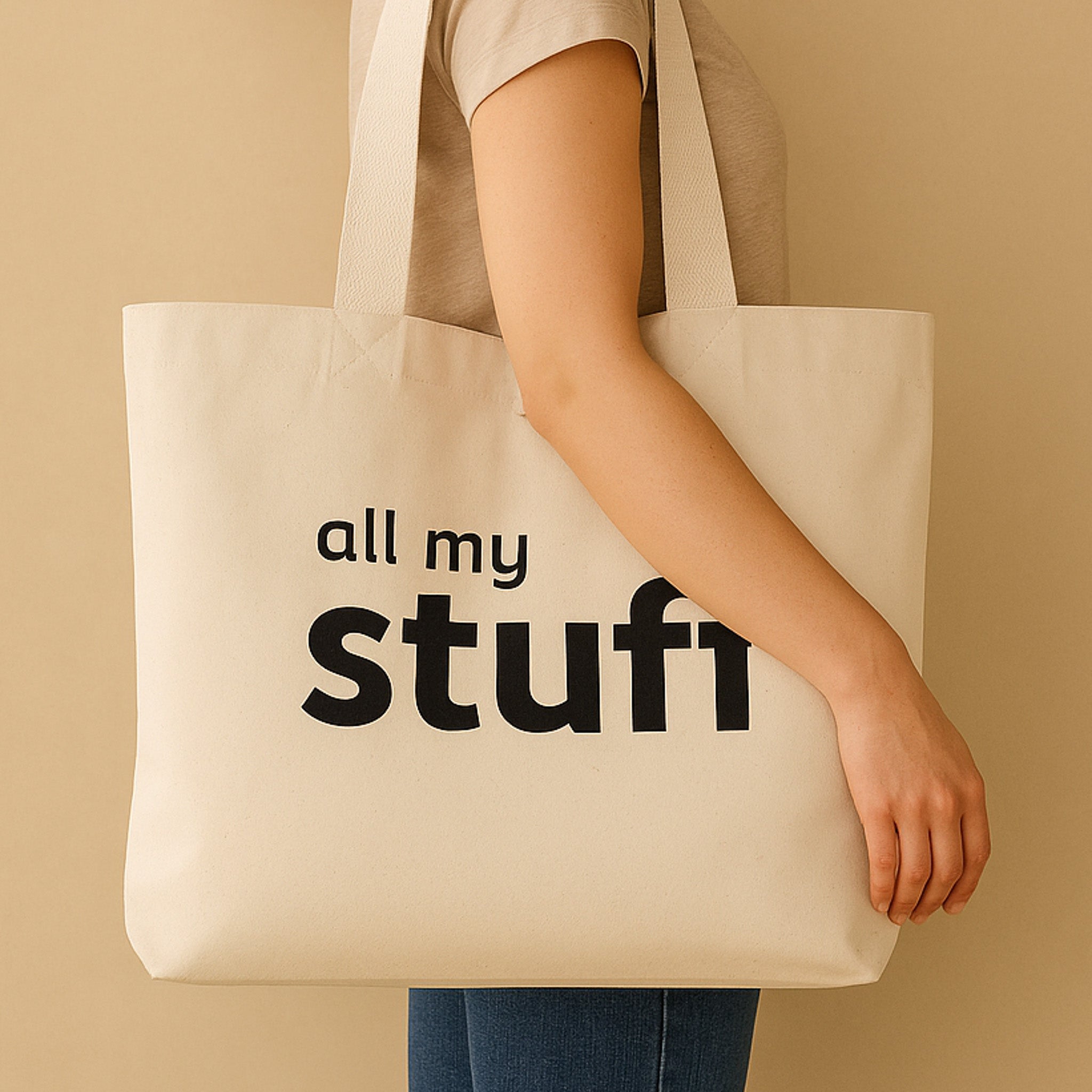 Person holding a natural tote bag with 'all my stuff' text on a beige background