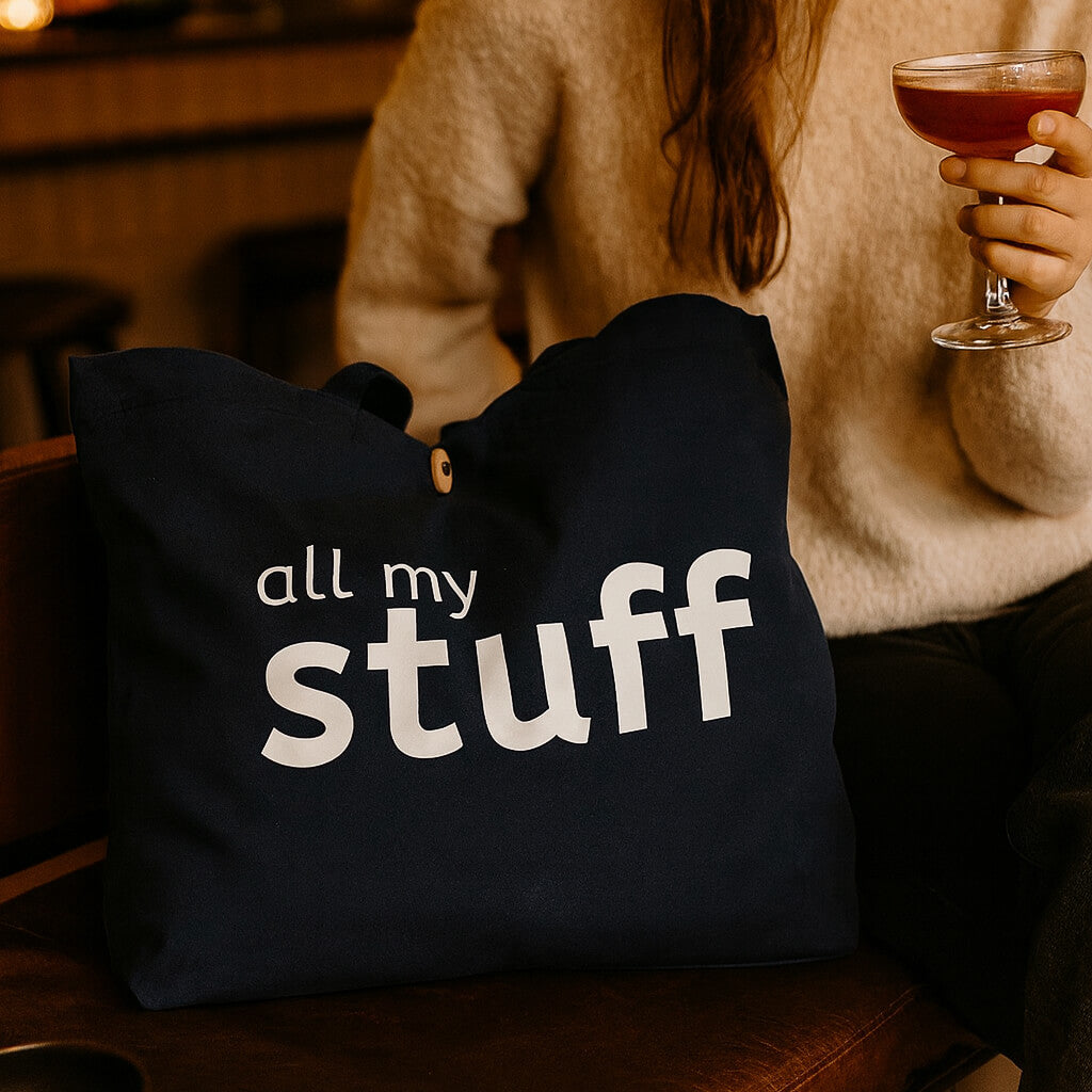 Person holding a glass of red wine next to a navy bag with 'all my stuff' text.