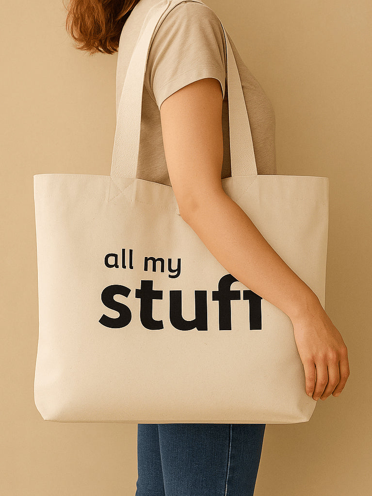 Person holding a natural tote bag with 'all my stuff' text on a beige background