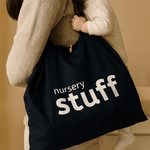 Person holding a baby with a navy bag with 'nursery stuff' text against a beige background